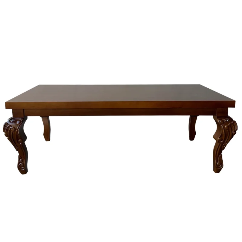 Visão em ângulo da mesa de centro de madeira maciça, evidenciando o brilho suave do tampo retangular liso e os profundos entalhes artesanais nos pés.